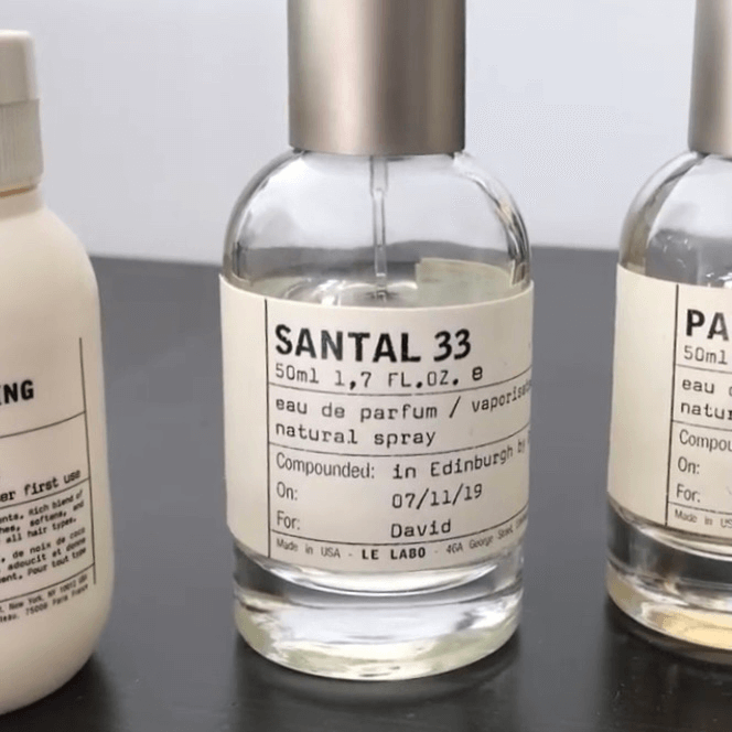 ル ラボ サンタル33香水瓶の画像。50ml サンタル33 オードパルファム スプレー瓶が中央に配置され、エディンバラで調香された'David'名義のカスタムメイド香水であることがラベルに表示されている。透明ガラス瓶にミニマルなタイポグラフィーが施され、左右には他のル ラボ製品も並んでいる。